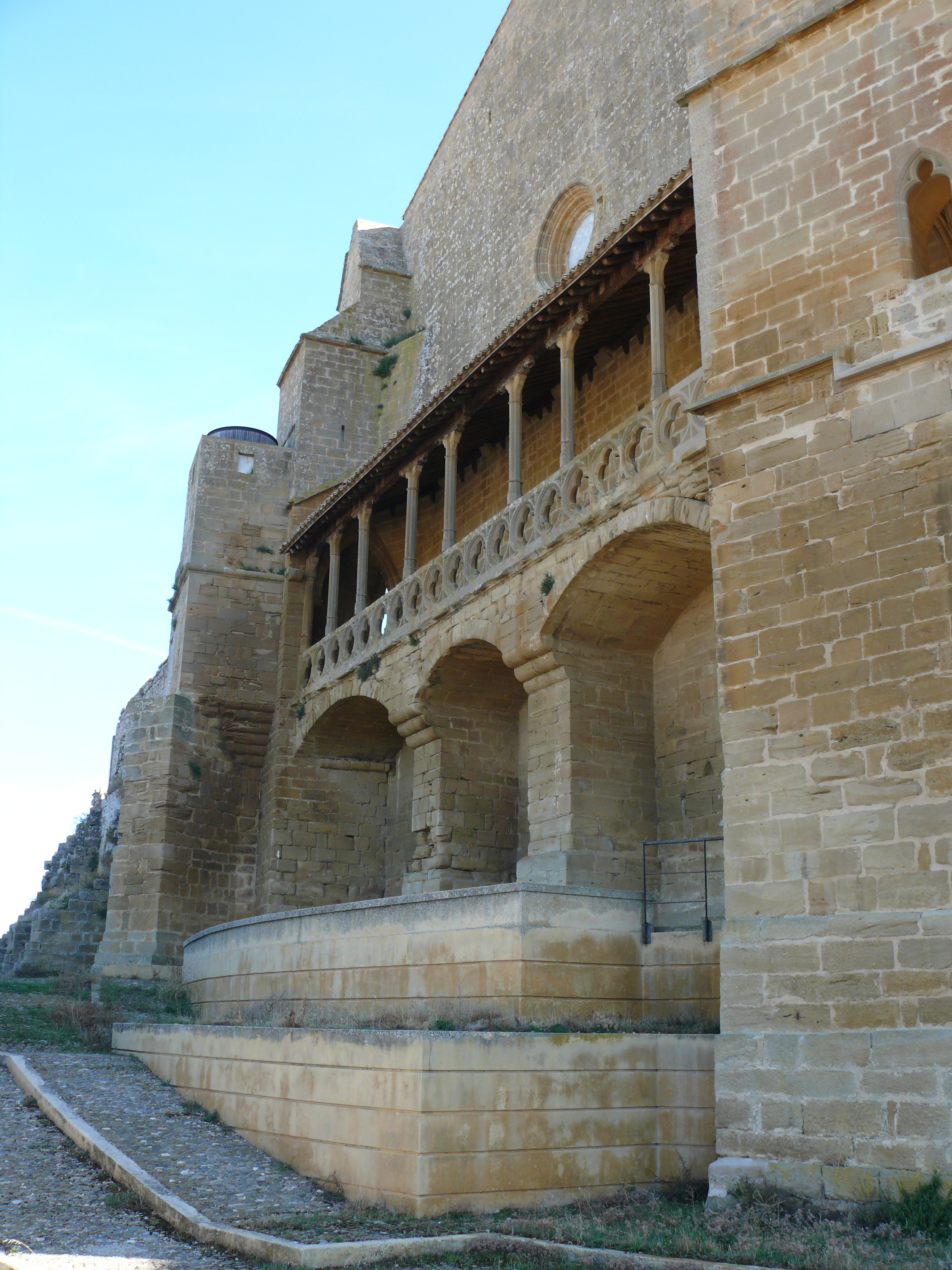 Vista del lado este del santuario. A la derecha, en primer término, aparece la base de la torre menor, en la que se ve el exterior de la ventana-mirador y, a continuación, una galería cubierta por la que continúa el paseo de ronda, hasta el final de este lateral.